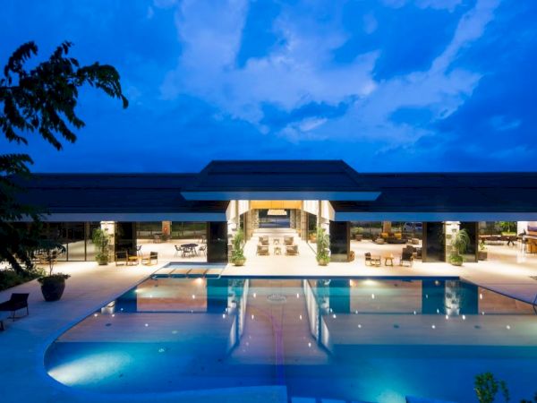 A luxurious, well-lit resort featuring a large swimming pool and outdoor seating areas under a twilight sky ending the sentence.