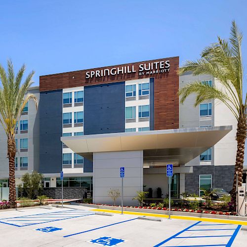 The image shows a Springhill Suites by Marriott hotel building with a modern facade, palm trees, and an accessible parking area in front.