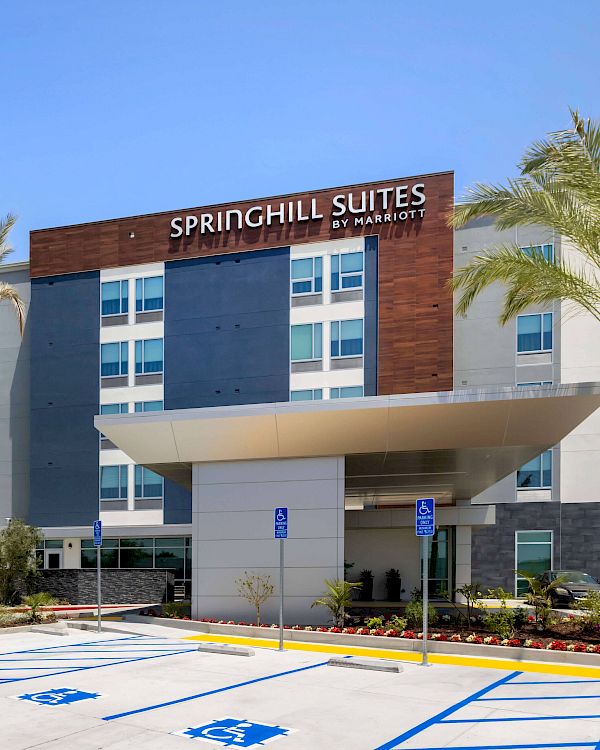 The image shows a Springhill Suites by Marriott hotel building with a modern facade, palm trees, and an accessible parking area in front.