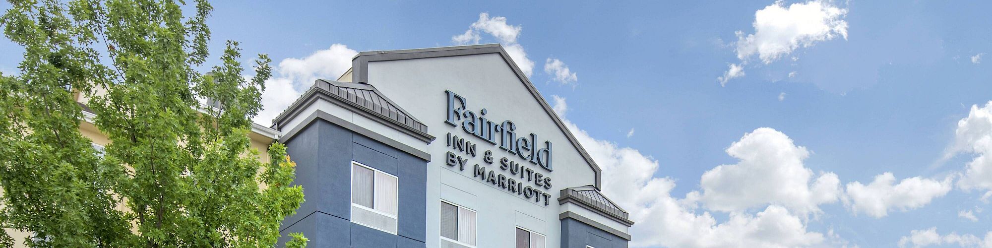 This image shows the exterior of a Fairfield Inn & Suites by Marriott hotel with a covered entrance and landscaped surroundings.