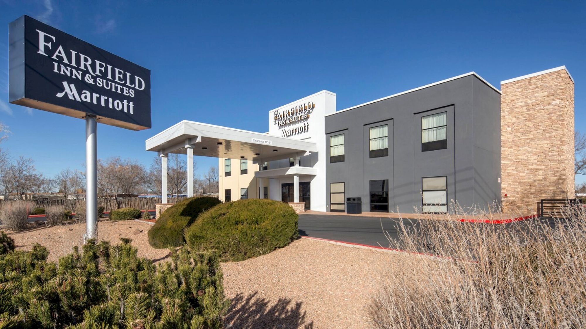 The image shows a Fairfield Inn & Suites by Marriott hotel building with clearly visible signage, surrounded by landscaping and a clear blue sky.