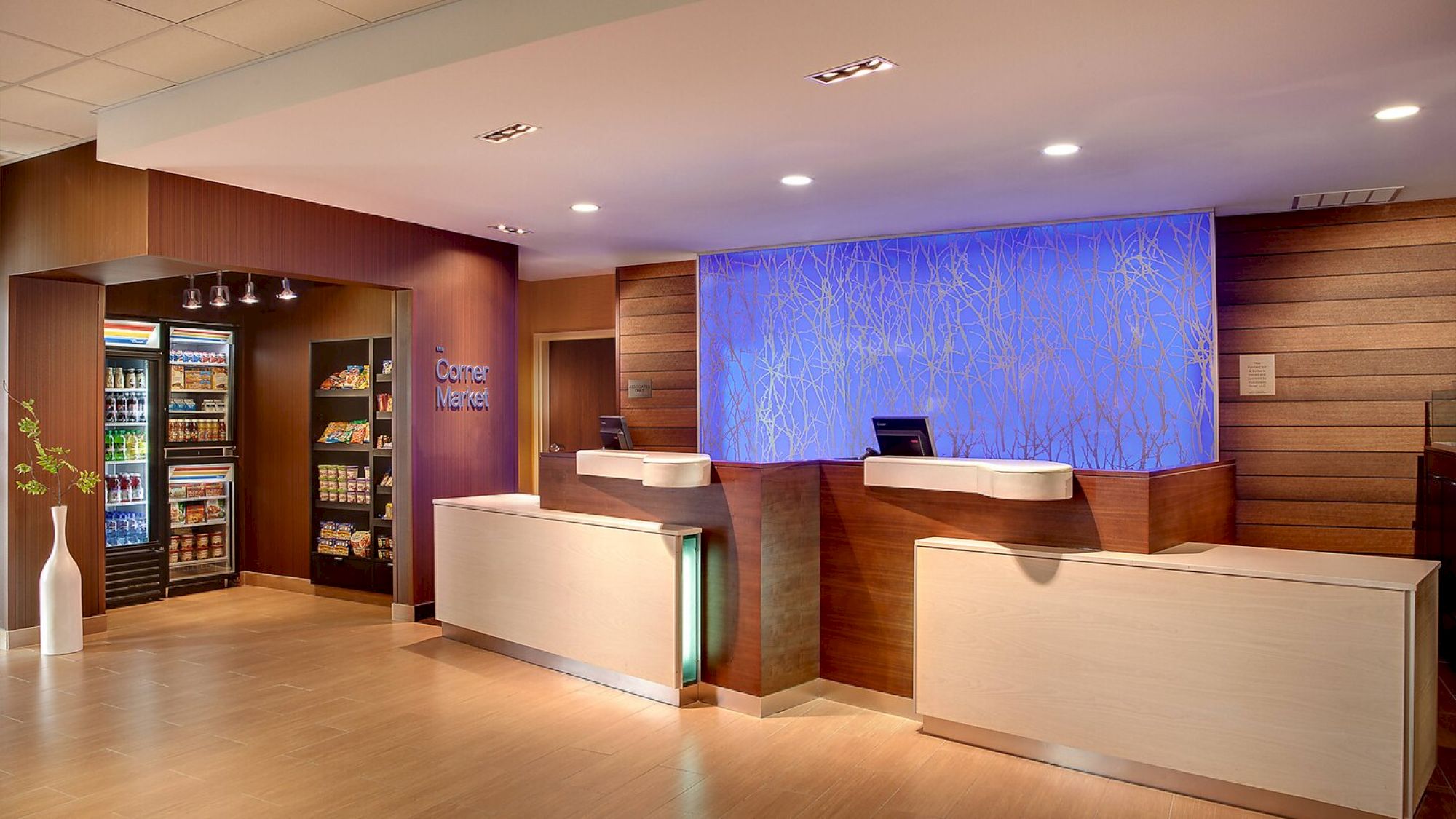 The image shows a modern hotel reception area with two check-in counters, a blue backlit wall, and a snack and beverage area on the left.