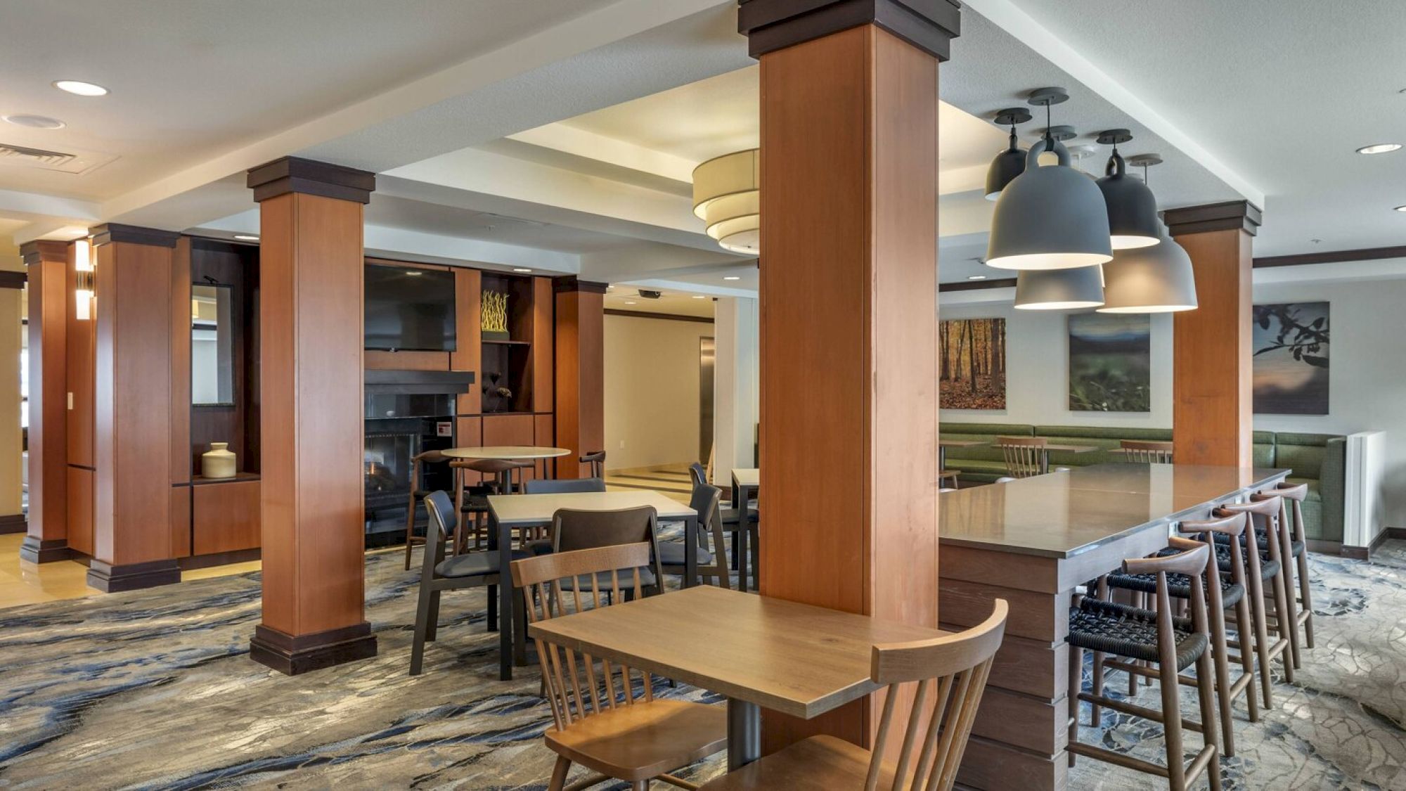 A modern indoor dining area with wooden furnishings, tables, and chairs, featuring hanging lights and framed art on the walls.