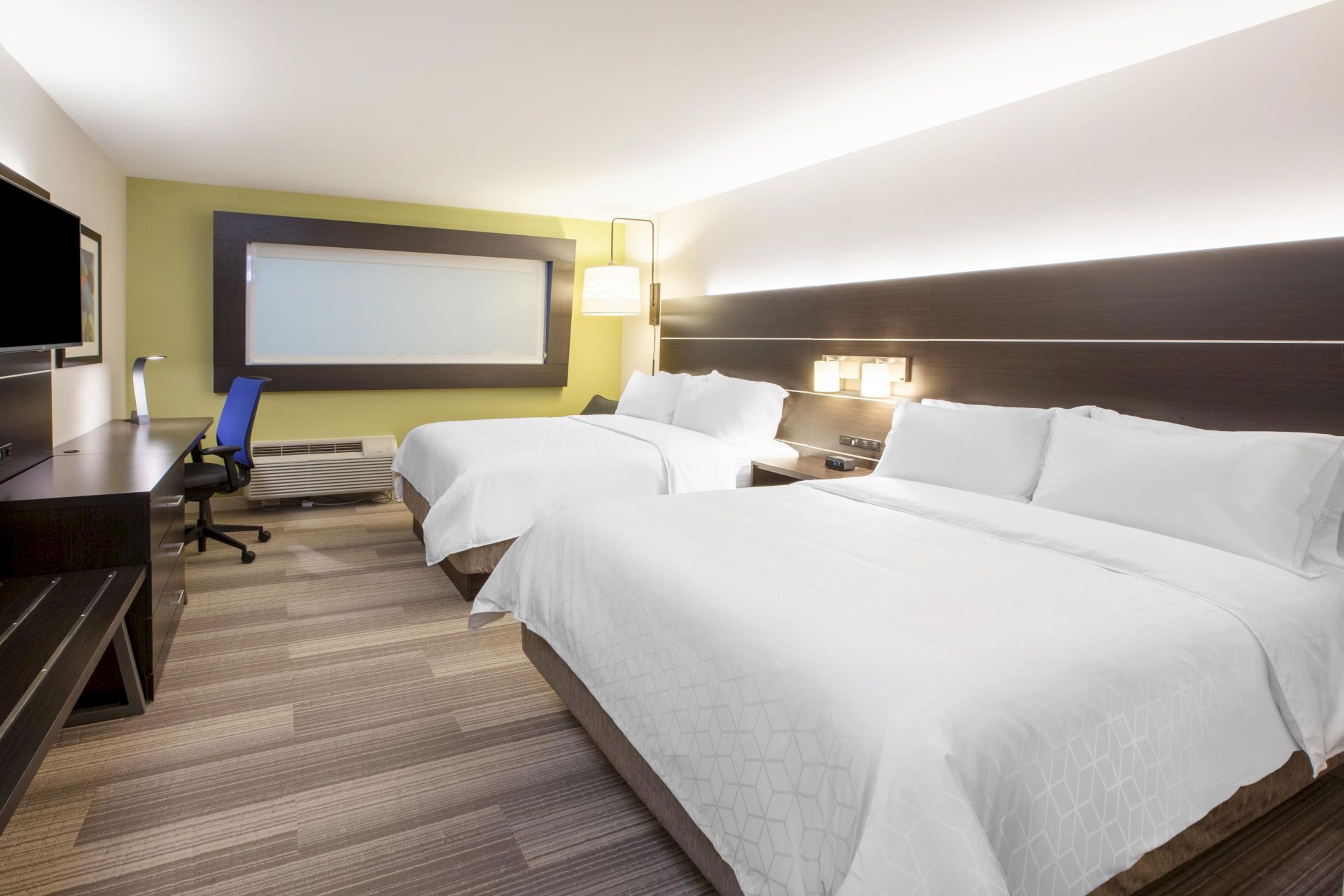 The image shows a modern hotel room with two double beds, a desk and chair, a wall-mounted TV, and contemporary lighting.