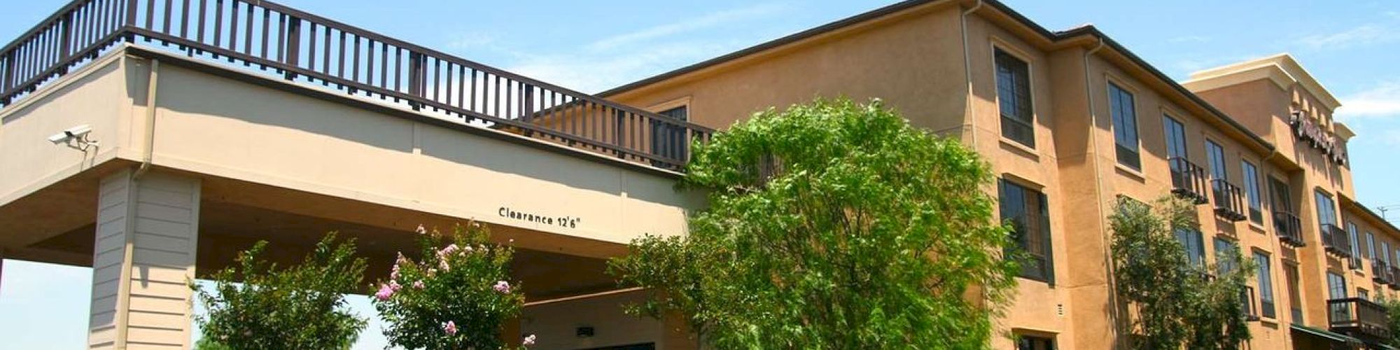 A three-story hotel building with a driveway, surrounding greenery, and clear skies in the background.