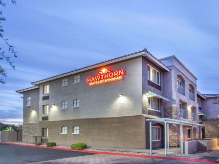 The image shows a building with a sign that reads "Hawthorn Suites by Wyndham" on the front, set against a mostly cloudy sky.