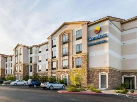 A multi-story hotel building with a sign that reads "Comfort Suites" and several parked cars in front of it.