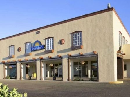 The image shows a Days Inn hotel building with a beige exterior, multiple windows, and a blue sign. There are hanging decorations below the windows.