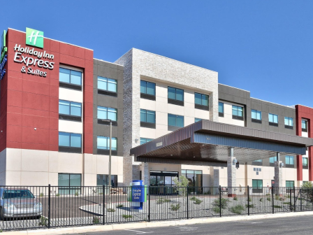 The image shows a modern Holiday Inn Express & Suites hotel building, featuring multiple windows and a car park area.