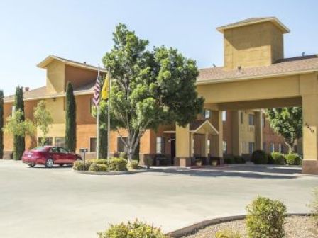 The image shows the entrance of a hotel with a car parked near the entrance, amidst trees and landscaped bushes.