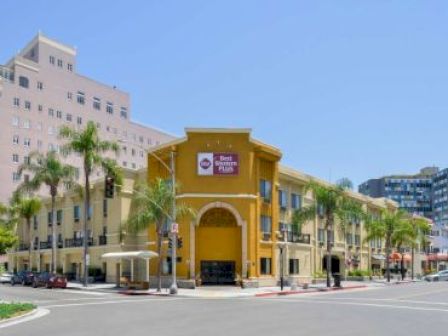 This image shows a Best Western Plus hotel on a street corner in an urban area with palm trees and nearby buildings.