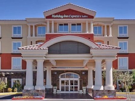 This image shows the front entrance of a Holiday Inn Express & Suites hotel with a large, welcoming portico and a clear blue sky.