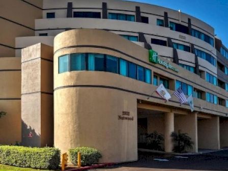 The image shows a multi-story hotel building with a modern architectural design, displaying the Holiday Inn logo and flags.