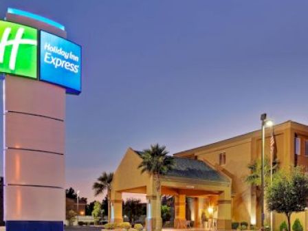 A Holiday Inn Express hotel is shown, with its illuminated sign and building entrance visible, surrounded by palm trees and evening lighting.