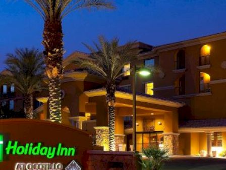 The image shows the exterior of a Holiday Inn hotel at nighttime, with illuminated palm trees and visible signage.