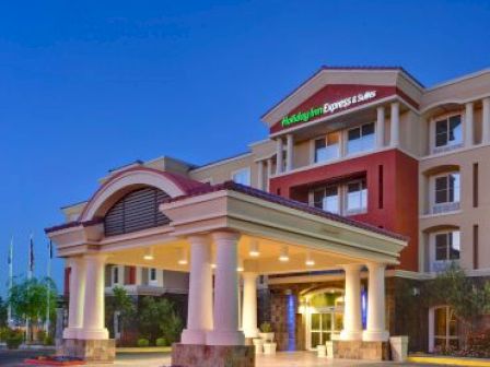 The image shows the exterior of a Holiday Inn Express & Suites hotel with palm trees and evening lighting.