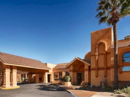 The image shows a building with Spanish-style architecture, featuring arches and a covered driveway, under a clear blue sky.