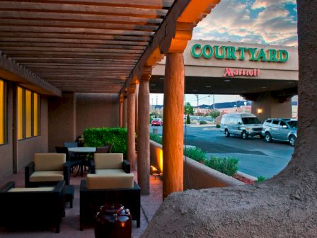 An outdoor sitting area with modern furniture, a covered walkway, and a view of a parking lot with cars. A "Courtyard by Marriott" sign is visible.