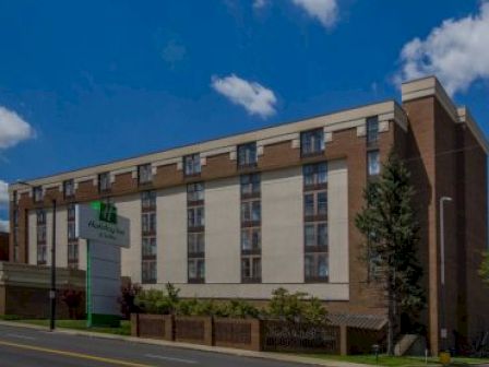 This image shows a multi-story hotel building with a Holiday Inn sign in front, situated along a street under a clear blue sky with scattered clouds.