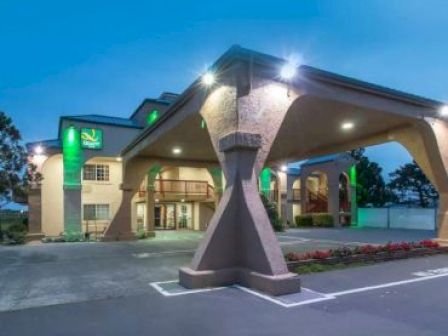 The image shows a hotel building with a large entrance canopy and exterior lighting. The structure has beige walls and green illuminations.