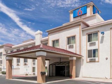 This image shows the exterior of a hotel building with a "6" logo, featuring an entrance canopy and multiple windows.