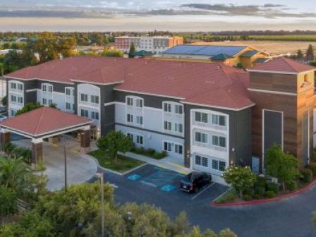 An aerial view of a multi-story building with a red roof, parking spaces, including handicapped spots, surrounded by trees and open landscape.