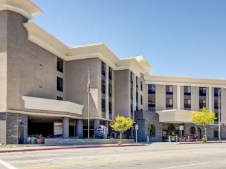 The image shows a modern, multi-story building with large windows, architectural features, and an American flag in front.