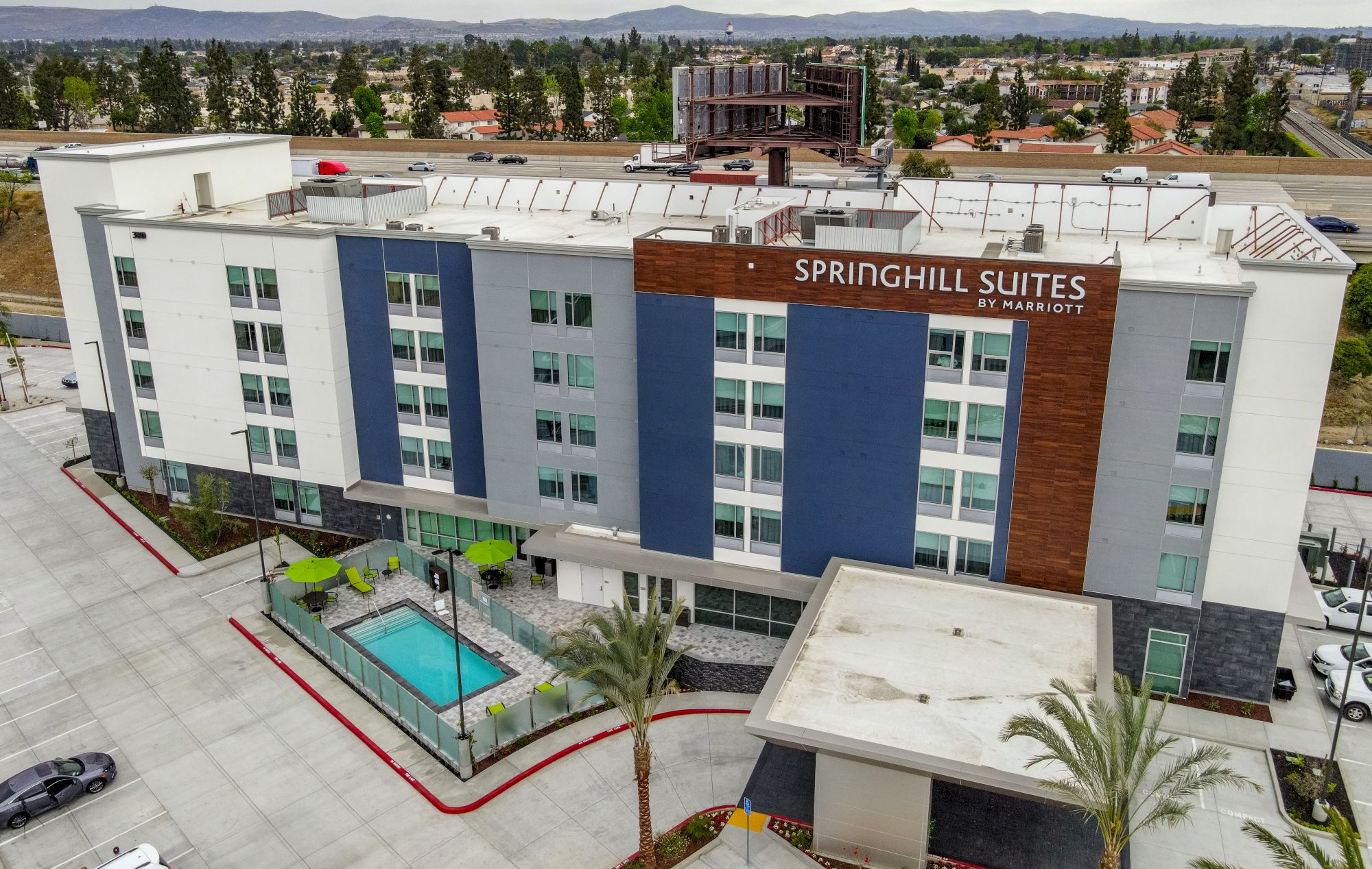 This image shows an exterior view of a hotel named "SpringHill Suites by Marriott," featuring a swimming pool, palm trees, and a parking area.