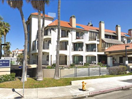 The image shows a multi-story hotel named "Huntington Beach Inn" with a Spanish-style architecture, located near palm trees and a road.