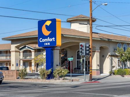 The image shows a Comfort Inn with a large sign, located at a street intersection with clear skies.