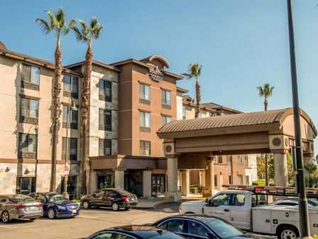 A multi-story hotel with a covered entrance, surrounded by parked cars and palm trees, under a clear blue sky.