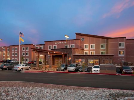 The image shows a hotel building with parked cars in front and a sunset sky in the background.