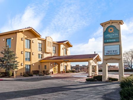 The image shows a La Quinta hotel with a sign offering free WiFi and breakfast, under a partly cloudy sky.