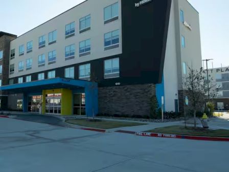 A modern hotel building with a colorful entrance is shown, with another building visible in the background.