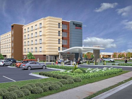 A modern hotel or conference center with a multi-story beige and brown facade, a long driveway, landscaped grounds, and a covered entrance.