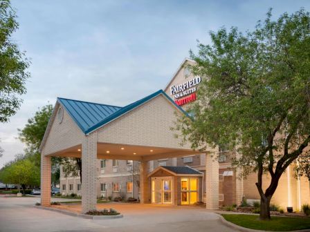 A Fairfield Inn & Suites hotel entrance with a blue-roofed building and &ldquo;FAIRFIELD INN & SUITES&rdquo; sign, surrounded by trees.